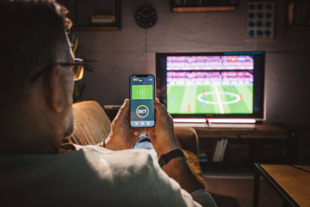 Watching soccer game at home Mature men sitting on sofa at home and watching soccer game.  He is using smart phone for sports betting . tv game stock pictures, royalty-free photos & images