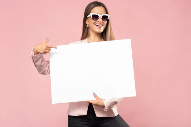 uma jovem feliz está segurando um pôster branco. - placard women blank holding - fotografias e filmes do acervo