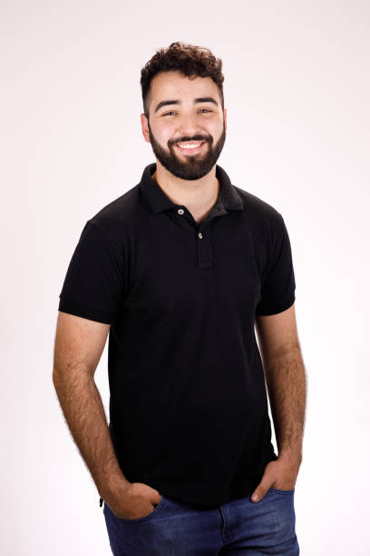 hombre barbudo con un polo negro sonriendo - manos en los bolsillos fotografías e imágenes de stock