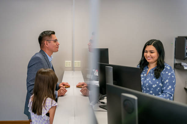 Latin American man and daughter checking in at office reception desk stock photo