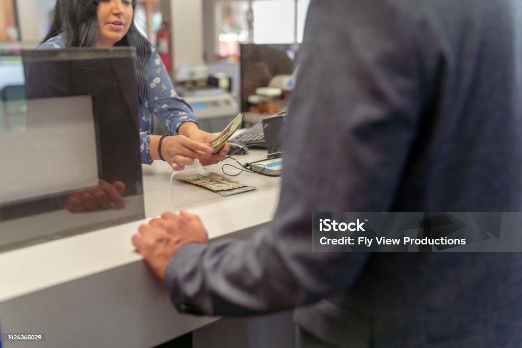 Bank teller counting money for customer Cropped shot of a female bank teller counting US Currency for a male customer at the counter in a bank. Selective focus on the bank teller's hands holding the money. Banking Stock Photo