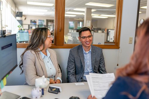 A Hispanic husband and wife smile while meeting with their financial advisor or banker about their budget and investments.