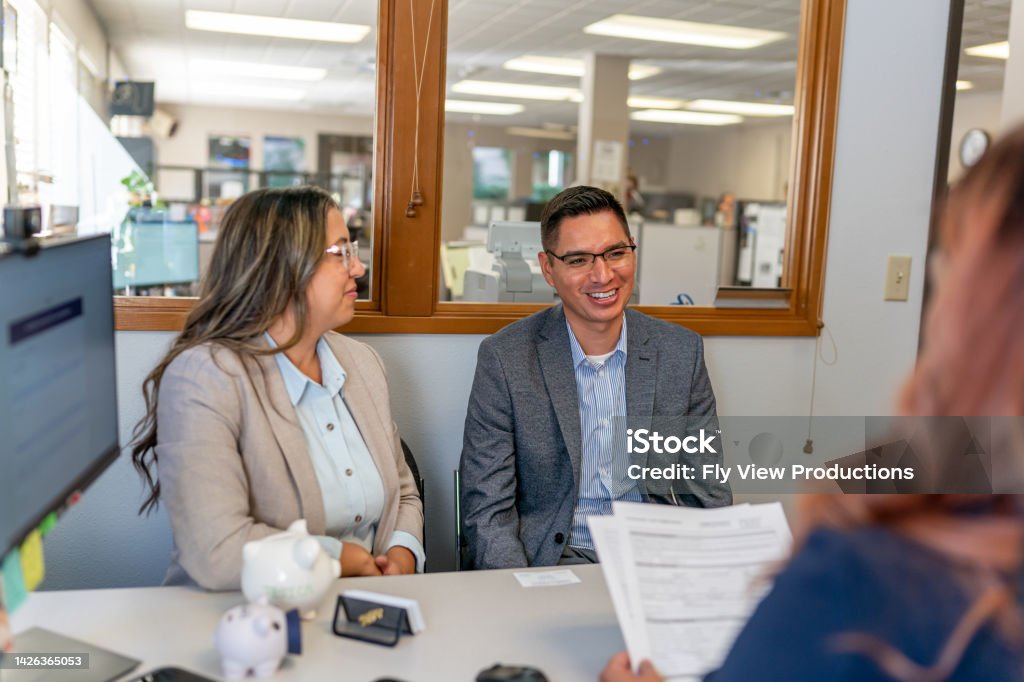 Cheerful Hispanic couple meeting with their financial advisor A Hispanic husband and wife smile while meeting with their financial advisor or banker about their budget and investments. Couple - Relationship Stock Photo