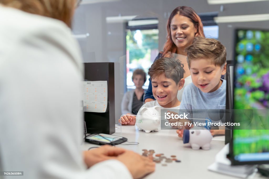 Mom teaching her sons about financial responsibility Two elementary age boys of Hispanic descent smile with excitement as a bank teller counts the coins they brought from their piggy banks. The children are learning about money and are opening a bank account with their mom's help. Bank Teller Stock Photo
