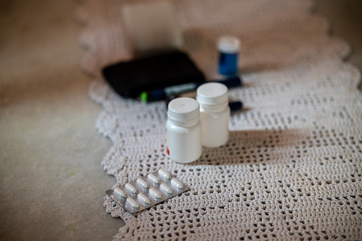 Photograph of some medicine pills, a blood pressure device and a glaucometer on a table.