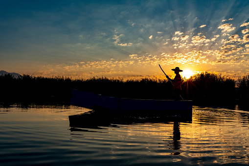 Fisherman silhouette in front of an early morning sunrise sky fishing out of his boat during a summer sunrise on lake