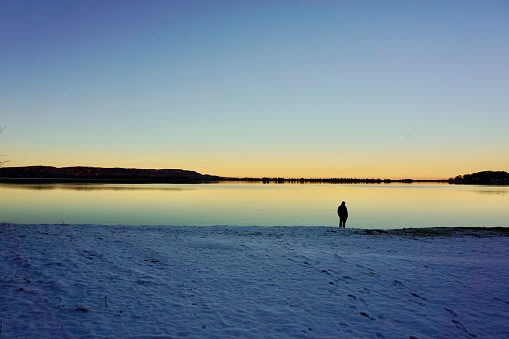 Colorful sunset in winter on the Walchensee. Sunset on the Bavarian lake. A bright sunset on a winter lake in Germany. A lonely man standing on the shore of a lake. The silhouette of mudchina standing by the lake at sunset.