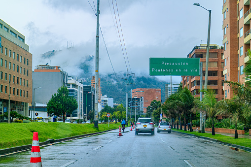 Bogota, Colombia - July 25, 2020: This is the Southbound carriageway of the usually busy Carrera 9 or 9th Avenue, in the Colombian Andes Capital city of Bogota. The section normally has bumper to bumper traffic at this time of the day. The lane on the left usually the fast traffic lane, has been blocked off for cyclists. It is to become a permanent cycle lane. It has been raining and low clouds cover the Andes Mountains in the backgroud. The altitude at street level is 8,660 feet above meamn sea level. Driver's Point of View. Horizontal Format.