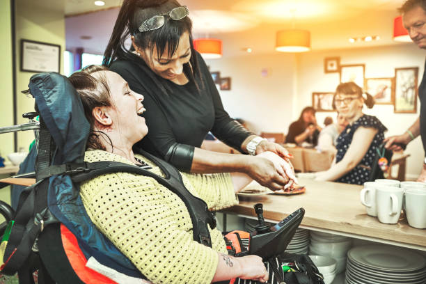 Wheelchair down syndrome disability girl patient in clinic or hospital with nurse or professional healthcare worker. Nursing and medical caregiver helping happy, friendly and young disabled person stock photo