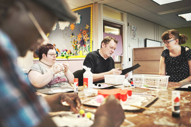Disability health care art workshop, creative paint and down syndrome people doing a project. Disabled painter group relax working with craft tools to do a special needs painting with a brush