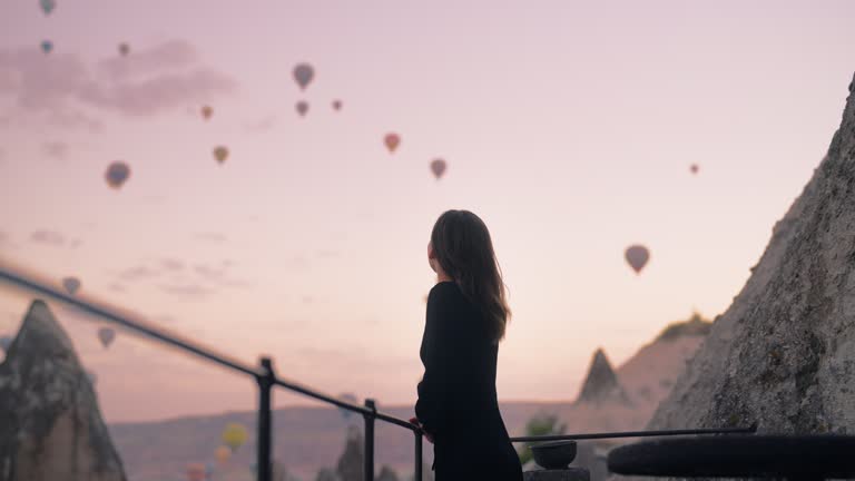 Female tourist enjoying watching hot air balloons flying in the sky at rooftop of hotel where she is staying during her vacation