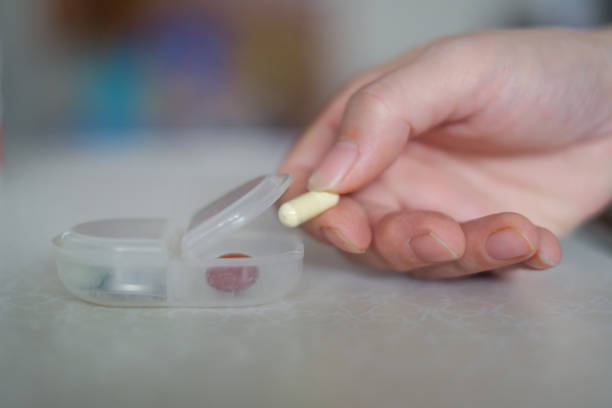 A person is holding a pill in their hand. The pill is white and is in a plastic container