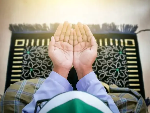 Photo of Top view man with praying hands sit on praying mat.