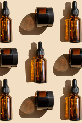 Mockup of amber glass bottles and cans are arranged in chaotic manner on beige background with hard shadow on surface. Unmarked packaging for cosmetics close-up. Top view, flat lay. Vertical image.