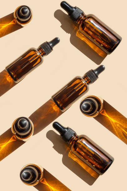 istock Bright pattern of from cosmetic makeup products on brown background with hard shadow. Amber glass jars with dropper lid for serum. Vertical image, close-up. Concept of mockups 1426447078