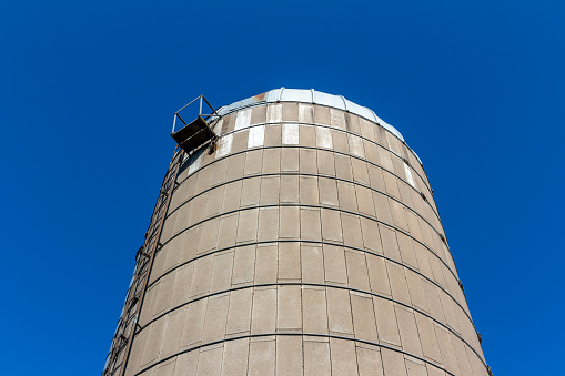 This image shows a low angle abstract texture view of a rustic old concrete silo wall with blue sky background, showing natural weathering from aging.