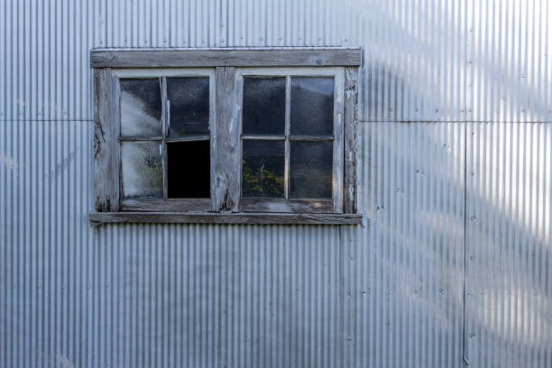 This image shows an abstract texture background of a rustic old wood framed glass window on a corrugated metal shed wall, with a grungy shabby chic appearance.