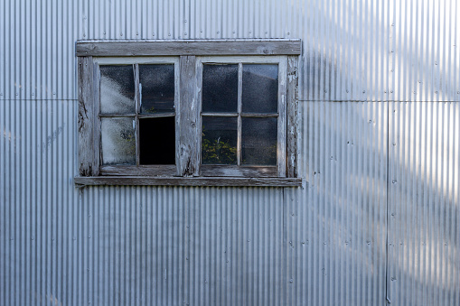Grungy old window on a corrugated metal shed wall