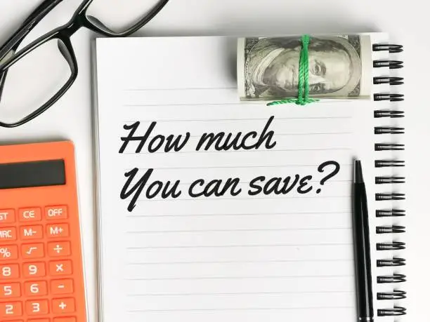 Text how much you can save written on note book with a pen,fake money,calculator and eye glasses.