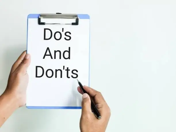Hand hoding a pen pointing on paper clip board written do's and don'ts.
