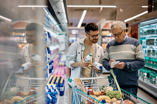 Senior man and his son buying groceries from their shopping list in supermarket. Copy space.