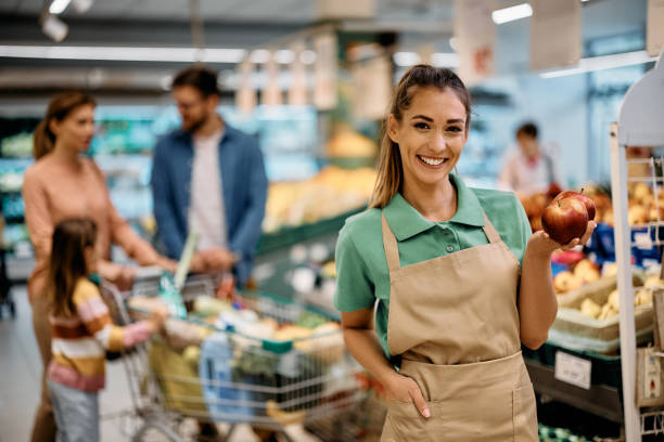 Happy supermarket employee holding apples while working at fruit section. stock photo