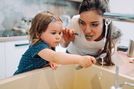 Shot of a smiling young mother and her cute little daughter brushing their teeth together at home. Mother shows her little girl how to brush her teeth properly.