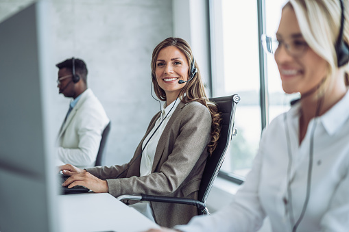 Shot of call center operators working in the office. Female call center agent working with her colleagues in modern office. Smiling beautiful businesswoman working in call center.