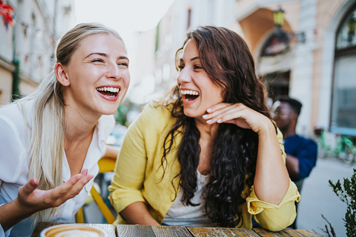 Shot of young happy women talking and laughing while drinking coffee together in a sidewalk cafe.