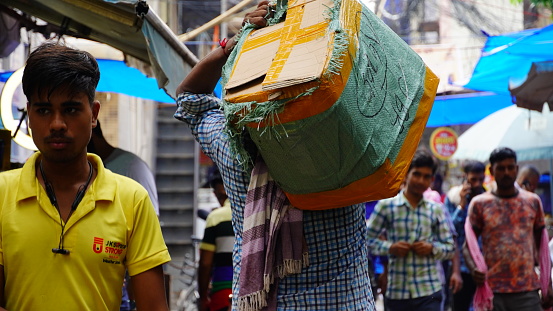 Nangloi, Delhi, India- 24 August 2022:Select focus on the laborer carrying goods on his shoulder