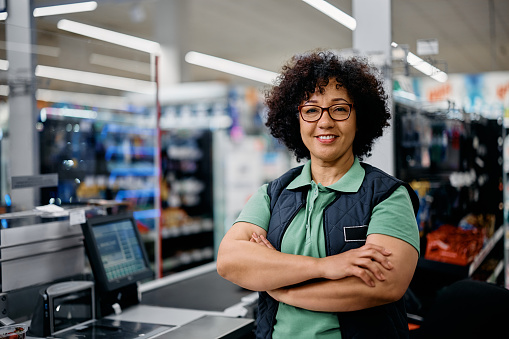Happy supermarket cashier with her arms crossed looking at camera.