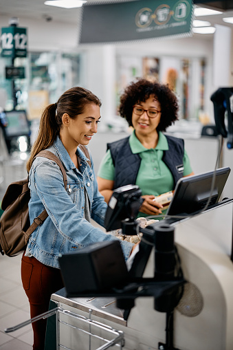 Supermarket worker assisting a buyer in using self-service till at checkout. Focus is on buyer.