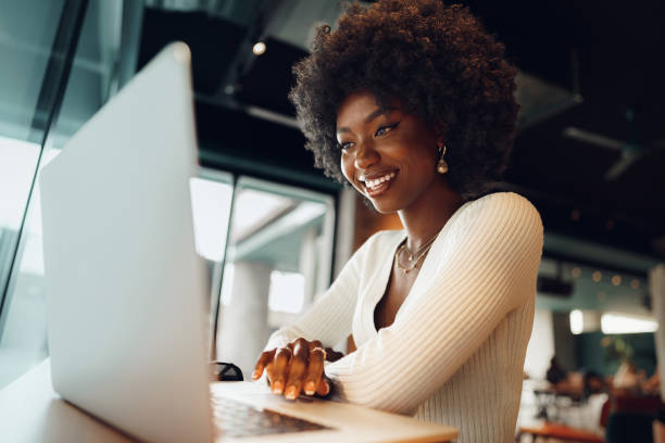 Smiling young african woman sitting with laptop in cafe stock photo