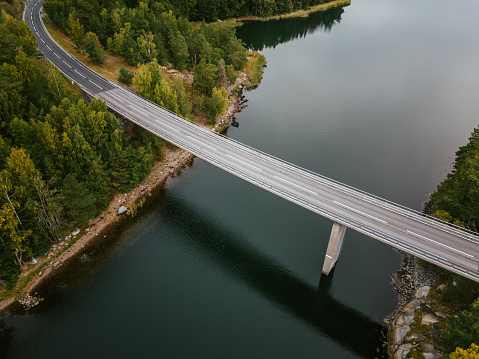 Drone point of view of empty road bridge over bay of water in Nordic nature.