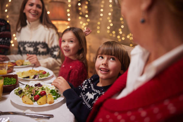 istock Happy boy talking to his family while having New Year's dinner at dining table. 1426469198
