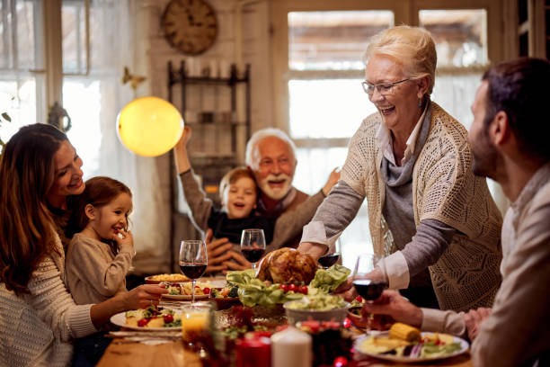 donna anziana felice che serve un pasto alla sua famiglia nella sala da pranzo. - family dinner eating meal foto e immagini stock