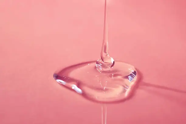 A drop of body gel or shampoo pouring from above on a pink saturated background.