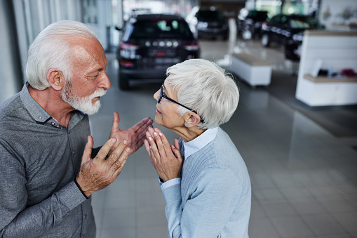 Senior woman begging her husband to buy a new car in a showroom.