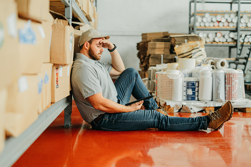 Burnout, headache and logistics businessman thinking in delivery, shipping or storage warehouse company. Stress, anxiety and tired employee in with checklist or inventory in supply chain industry