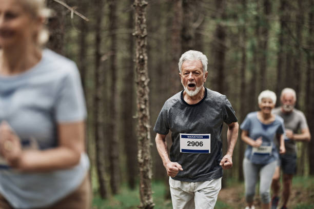 Mature man and other seniors running a marathon race in the forest.