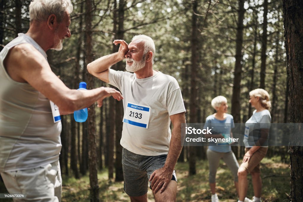 Ugh, I'm exhausted! Happy senior man talking to his friend after exhausting marathon race in nature. Active Lifestyle Stock Photo