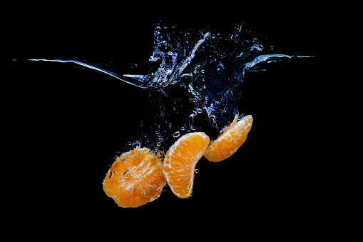 Close-up of tangerine slices sinking underwater with splashes isolated on black background.