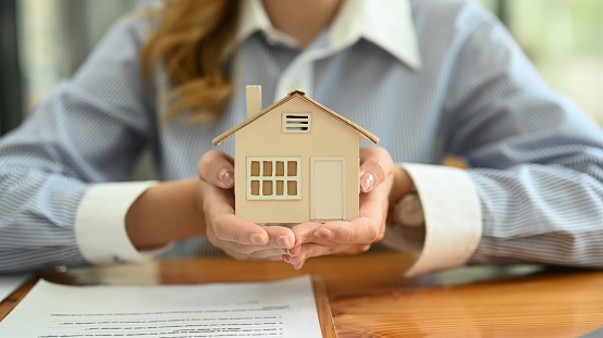 Cropped imaged of young woman hands holding small house model. Real estate investment, purchase and sale.