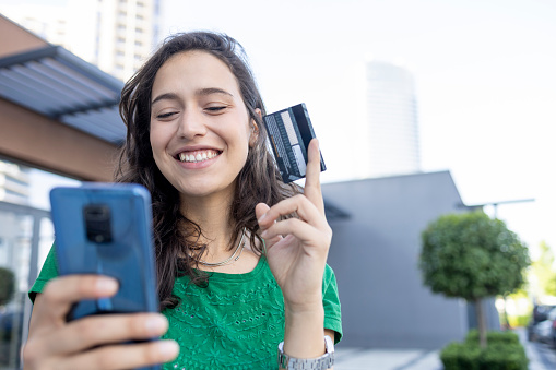 Close-up of a happy young woman standing on the street and purchasing online
