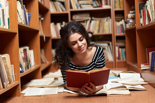 Attractive young woman in striped top and black mini skirt in a library full of books, posing as a librarian or student