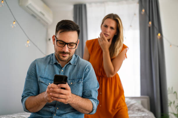 jealous woman spying boyfriend and watching his mobile phone. couple cheating jealousy concept - inveja imagens e fotografias de stock