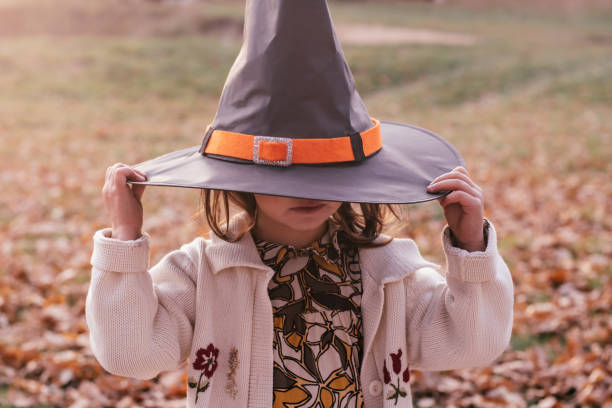 menina de 3 a 4 anos fica ao ar livre em parque no outono folhas de carvalho caído e puxa chapéu de bruxa de halloween sobre os olhos - preschool 2 3 years preschooler little girls - fotografias e filmes do acervo