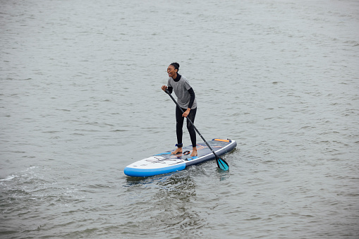 A shot of a young woman learning how to paddle board in the sea, she is smiling in Northumberland.