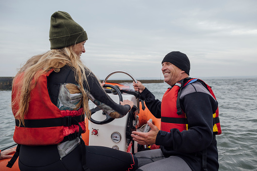 A shot of an instructor teaching a member of staff how to sail a dinghy boat in the sea, they are wearing safety life jackets in Northumberland.
