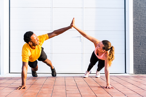 Interracial sportive couple training outdoors - Multiracial couple wearing sportswear and doing functional workout outdoors to strenght body muscles, core abs, stamina and cardio